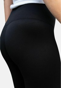 Svarta ribbade leggings med h�ög midjeresår, med en slät textur och figurnära design, fotograferade bakifrån.