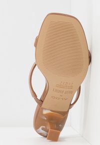 Brun klacksandaler med en strukturerad, glänsande yta. Har en fyrkantig tå och ett smalt vristband. Sulan har ett ribbat mönster för bra grepp.