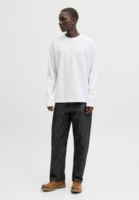 Langærmet hvid bomulds-T-shirt kombineret med teksturerede sorte denimbukser og brune snørebåndsstøvler. Simpelt design, afslappet pasform.