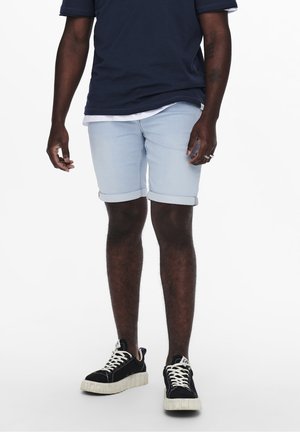 Light blue denim shorts with rolled cuffs, paired with a navy t-shirt and black platform sneakers with white laces. Minimalist design.