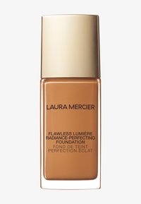 Fondación Laura Mercier en un frasco de vidrio transparente con una tapa dorada, presenta un líquido ámbar suave y texto negro que etiqueta el producto.