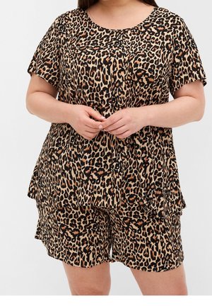 Mujer con un conjunto de top de manga corta y pantalones cortos con estampado de leopardo marrón y negro, de pie con las manos entrelazadas en la cintura.