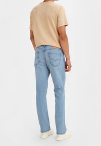 Light beige short-sleeve t-shirt paired with light blue jeans. The jeans feature back pockets with stitching and a brand label on the waistband.