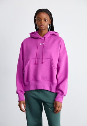 Sweatshirt à capuche rose avec une poche avant, arborant un logo blanc et des cordons. Porté avec un pantalon de survêtement vert affichant un logo.
