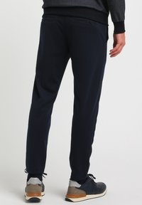 Marineblå joggerbukser med slim fit, elastisk talje, sidelommer og en glat stofstruktur. Matchet med sorte og grå sneakers.