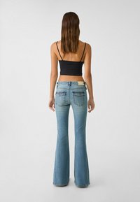 Tight sort sort sort og sort top og lyseblå flared jeans med en lysvasket effekt. Jeansene har to baglommer og et tan-lædermærke på taljen.