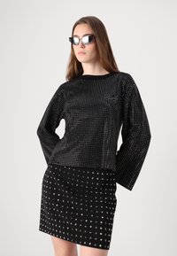 Juodas viršus su metaliniais spaudais, ilgos rankovės; derinamas su juoda mini sijonu, taip pat su sidabriniais spaudais. Aksesuarai - kampuoti saulės akiniai.