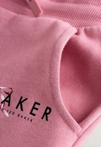 Roza džemper s mekanom pletenom teksturom, okruglim izrezom i crnim "BAKER" natpisom sprijeda. Vidljive su šavanje.