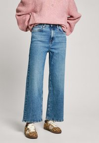 Jeans de pierna ancha en azul claro con cintura alta, que cuentan con un diseño de cinco bolsillos y un dobladillo limpio. Combinados con zapatillas de estampado de leopardo.