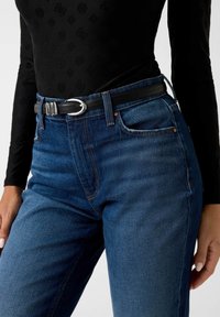 Jeans di denim blu a vita alta con tasche frontali, leggero effetto usurato, cuciture arancioni e una cintura nera con fibbia argentata.