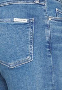 Vaqueros de mezclilla azul con un corte clásico. Presentan un bolsillo trasero con una etiqueta y un detalle de costura. La tela tiene una textura suave.