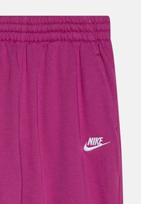Fuksijas sporta bikses ar elastīgu jostu, sānu kabatām un baltu Nike logo tuvumā kreisās kabatas, ar mīkstu tekstūru.