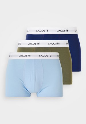 Three pairs of boxers: light blue, olive green, and navy, with a white waistband featuring "LACOSTE" printed in black. Cotton material, standard cut.