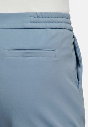 Pantalon bleu clair avec ceinture élastique et une poche arrière horizontale cousue à plat contre le tissu.