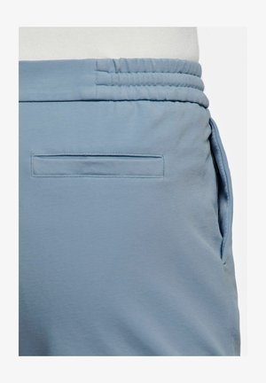 Pantalon bleu clair avec ceinture élastique et une poche arrière horizontale cousue à plat contre le tissu.