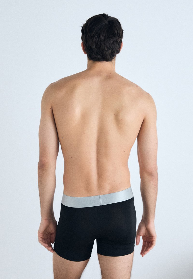 Boxer shorts noirs avec une ceinture argentée, présentant une texture douce et extensible ainsi qu'un design ajusté, vus de dos.