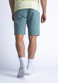 Mannelijke teal shorts met omgeslagen zoom, gecombineerd met witte sokken en Reebok sneakers. De stof lijkt glad, met een casual ontwerp, zonder zichtbare patronen.