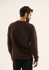 Brun sweatshirt med ribbad mudd och framkant, med en klassisk rund halsringning och raglanärmar; mjukt tyg och enfärgad.
