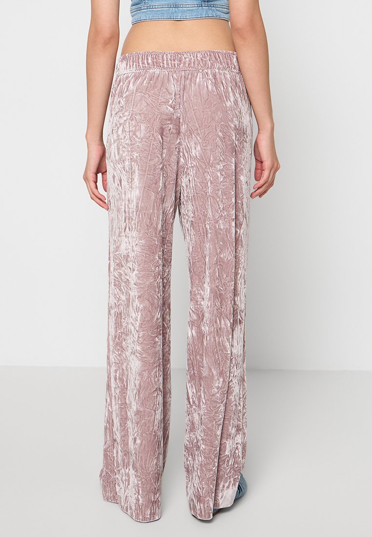 Jasnoróżowe szerokie spodnie z marszczonej tkaniny, z elastycznym pasem i zwiewnym krojem. Widok z tyłu ukazuje wzór materiału.