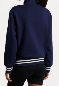 Navy pullover sweatshirt with a high collar, featuring white striped ribbed cuffs and hem, made of soft fabric with a relaxed fit.