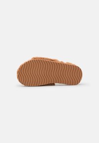 Fuzzy tan slipper with a textured brown rubber sole featuring wavy patterns, providing grip and comfort for indoor wear.