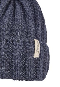 Knitted wool beanie in dark navy blue, featuring textured ribbed design and a small cream tag with brand name on the side.