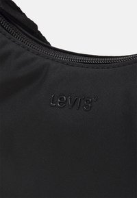 Musta kangas, jossa on teksturoitu pinta ja musta vetoketju. Tuotemerkin logo "Levi's" on painettu mustana lähelle vetoketjua.