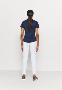 Navy blue, short-sleeved top, paired with white, slim-fit pants. The outfit is complemented by green and pink sneakers. Simple design.