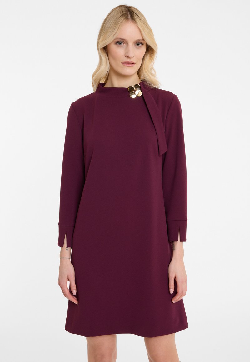 Maroon shift dress in a smooth fabric, featuring long sleeves, side slits, and a round neckline with a gold accent near the collar.