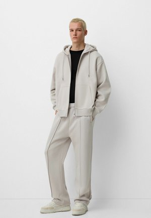 Light grey hoodie with drawstrings, paired with matching light grey sweatpants. Black t-shirt underneath. Textured fabric, relaxed fit.