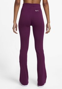 Leggings violets évasés avec une taille haute, en tissu extensible, dotés d'un petit logo Nike blanc à l'arrière. Texture lisse.