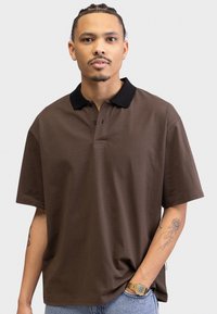 Brown polo shirt with a black collar, short sleeves, and a button placket. The fabric appears soft and has a smooth texture.