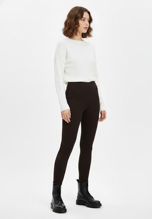 Schwarze gerippte Leggings kombiniert mit einem weißen gerippten Pullover, das Modell trägt schwarze geschnürte Kampfstiefel; glatte Textur und figurbetontes Design.