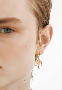 Pendientes de gota de oro con un diseño en forma de diamante que presenta patrones intrincados y tres pequeños acentos colgantes. Superficie suave y pulida.