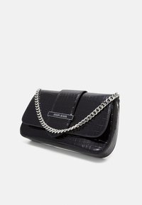 Pochette noire en croûte de cuir brillant avec une sangle en chaîne argentée et une plaque en métal rectangulaire portant l'inscription "JOOP! JEANS" sur le rabat avant.