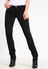Jeans ajustados negros con una textura suave, diseño de cinco bolsillos y botón plateado en contraste. Combinados con botas altas negras de tacón.