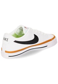 Zapatilla blanca con swoosh negro, acento naranja y cuero texturizado. Presenta una suela de goma y franjas negras en la parte inferior.