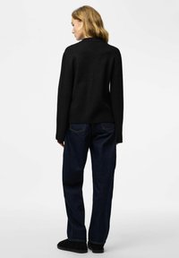 Maglione nero lavorato a maglia con una vestibilità comoda, abbinato a jeans a gamba larga di colore blu scuro. Il maglione presenta una scollatura semplice e maniche lunghe.