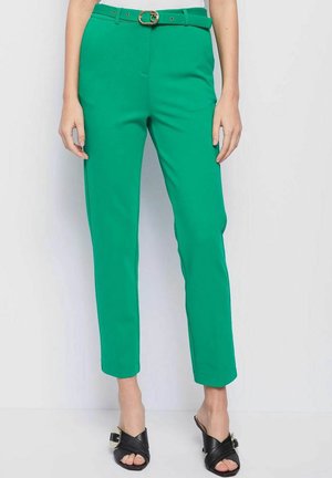 Groene, op maat gemaakte broek met een riem met een gouden gesp, taps toelopende benen, gladde textuur en zijzakken, gecombineerd met zwarte sandalen.