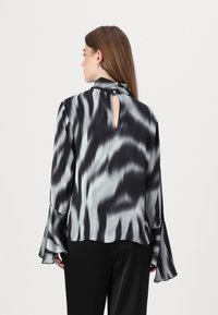 Svart og grå tie-dye bluse med høy krage og nøkkelholåpning bak. Har flagrende ermer og knappdetaljer ved halslinningen. Silkeaktig tekstur.
