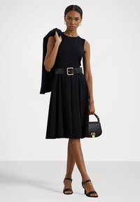 Melnas bezpiedurkņu kleitas ar piegulošu augšdaļu un izplestu svārku, ar plašu jostu, kas sašūta viduklī un rotāta ar zelta sprādzi. Melnas rokassomas un sandales.