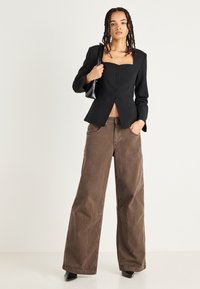 Melna strukturēta bleizera ar kvadrātveida dekoltē, trijām pogām un garām piedurknēm. Kombinēts ar pārmērīgiem brūniem biksēm un mazu melnu rokassomu.