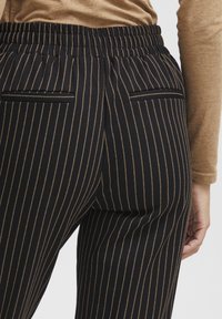 Pantaloni a righe nere e oro con vita elastica, dotati di due tasche posteriori e una texture di tessuto liscia.