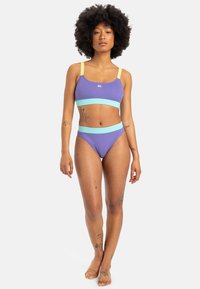 To-delt bikinis i ribbet stoff som har en lilla topp med lyseblå og gule detaljer, tilhørende høytlivde truser.