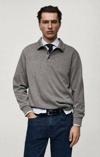 Grå långärmad polotröja med ribbad krage och treknäppning, bärs över en ljusblå skjorta, ihop med mörka denimjeans.