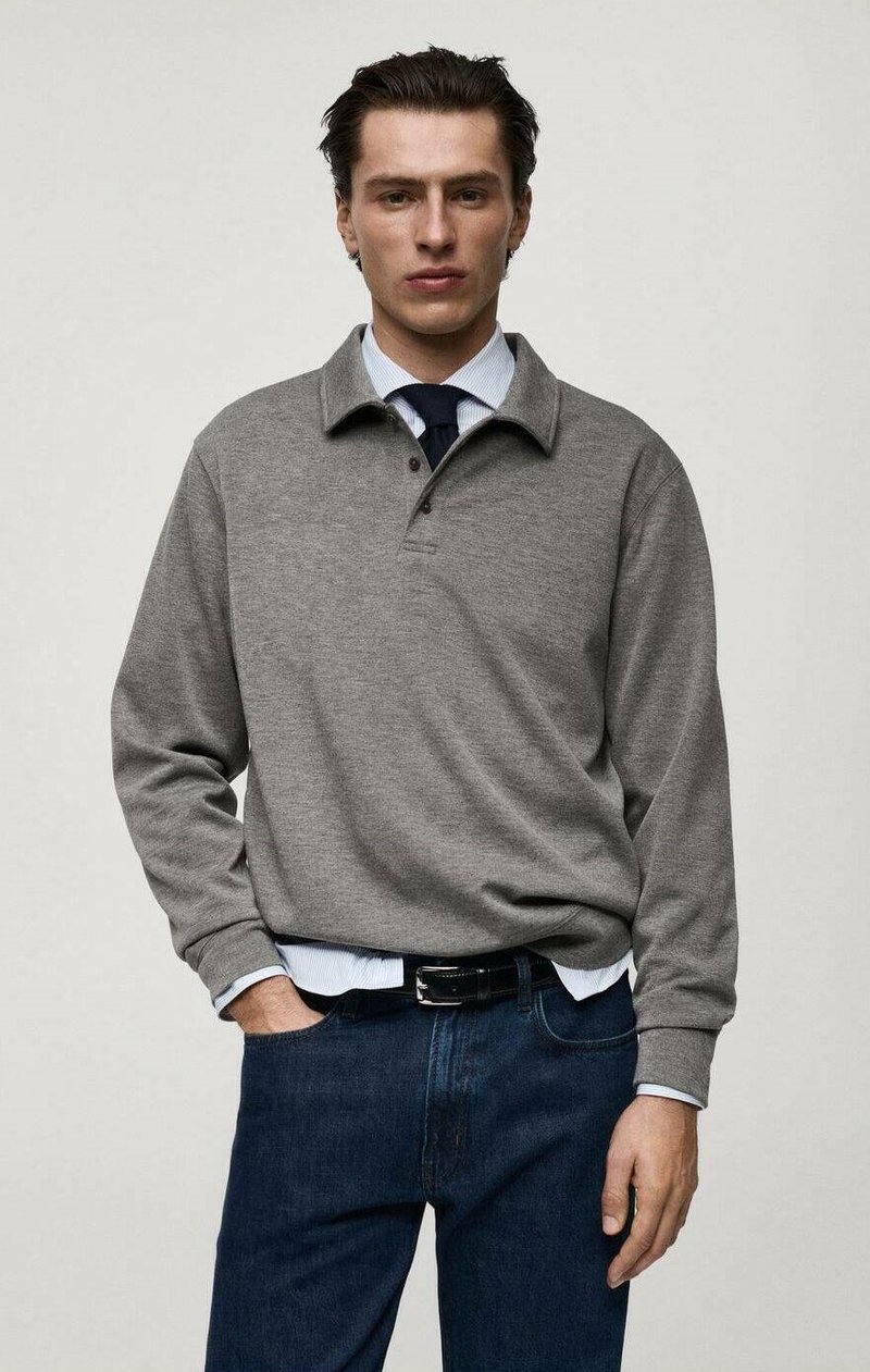 Grå långärmad polotröja med ribbad krage och treknäppning, bärs över en ljusblå skjorta, ihop med mörka denimjeans.