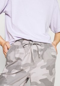 Pantalons camouflage gris à coupe décontractée avec taille élastique et cordon de serrage, fabriqués en tissu doux, avec poches latérales et texture subtile.
