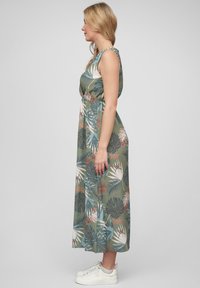 Floral maxi dress in green fabric featuring a tropical leaf pattern in blues, pinks, and whites. Sleeveless design with a waist tie.