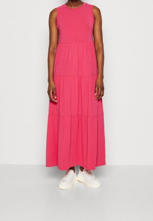 Person wearing a sleeveless, tiered pink maxi dress paired with white sneakers, standing against a plain white background.
