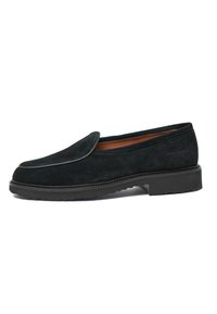 Black suede loafers with a rounded toe, contrasting piping, and a textured rubber sole. Features a minimalist design and flat heel.